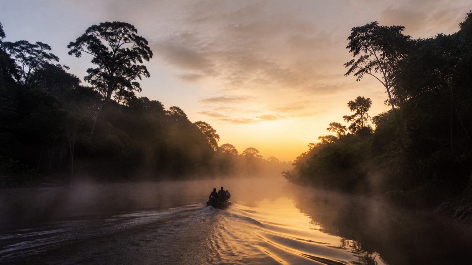 A small wooden boat heading upriver at dawn through heavy mist
