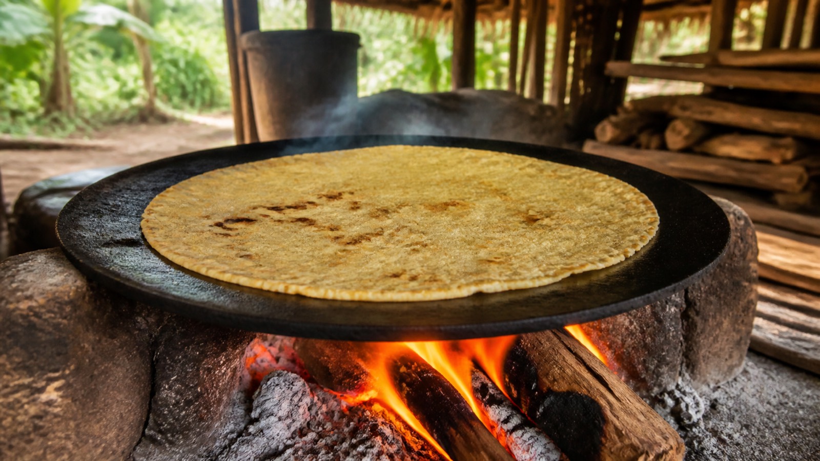 Rounds of cassava bread cooling beside a traditional fire-heated griddle