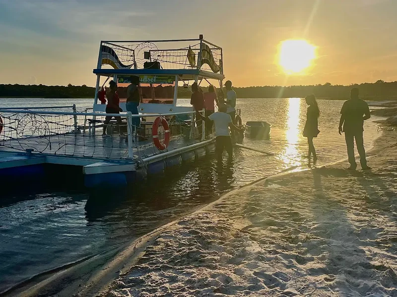 Silhouetted visitors stand beside a moored boat in golden sunset light.