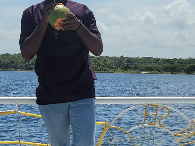 Hands holding a fresh green coconut beside the river, with the person’s face outside the crop.