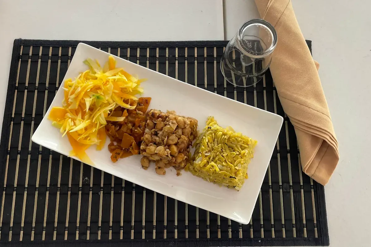 A rectangular plate of cooked food and shredded vegetables on a woven placemat.