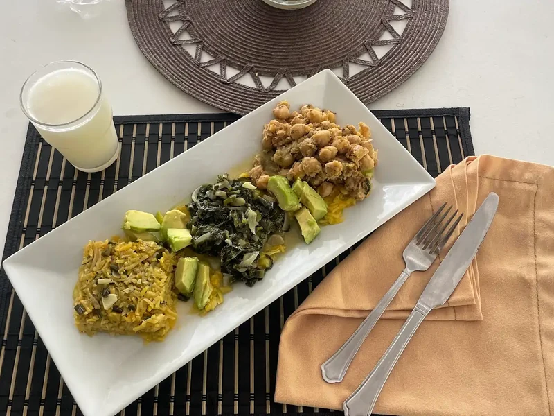 A rectangular plate with several cooked dishes and vegetables beside cutlery and a drink.