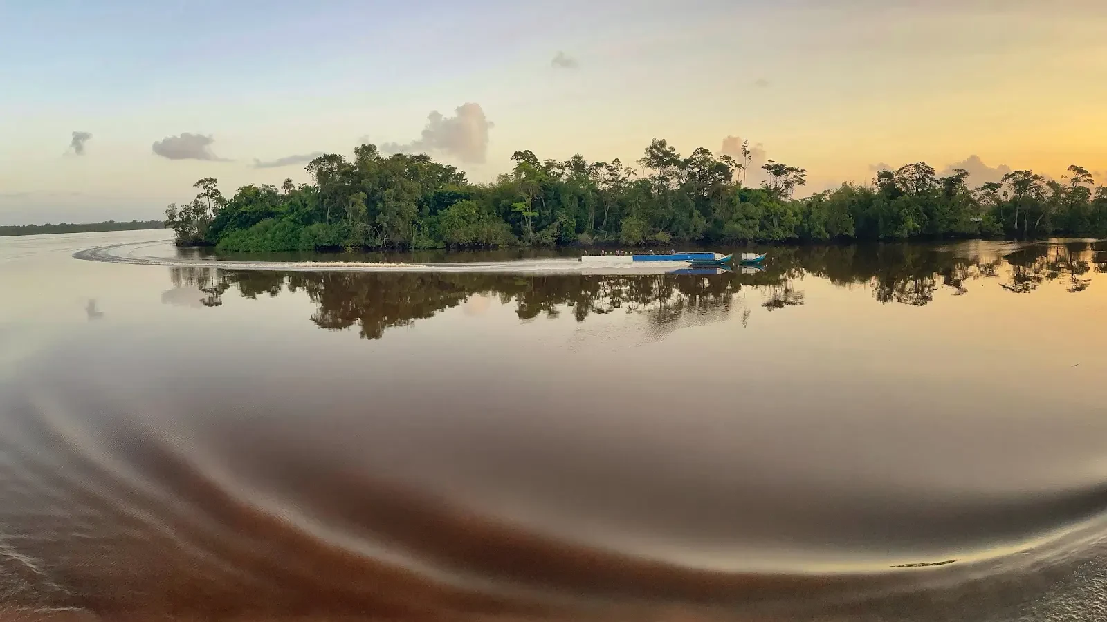 Two small boats leave curved wakes in a calm river reflecting trees and evening light.