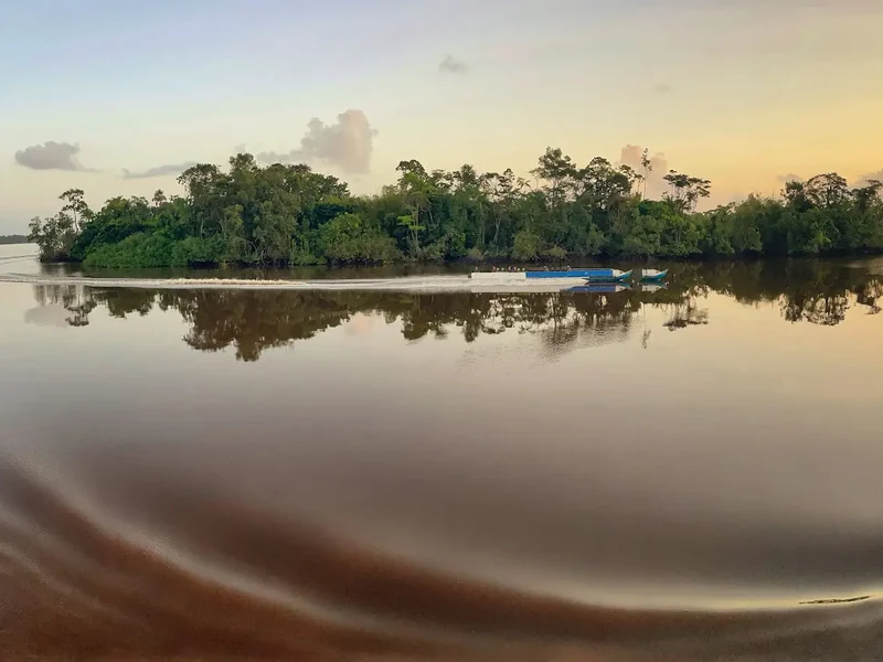 Two small boats leave curved wakes in a calm river reflecting trees and evening light.