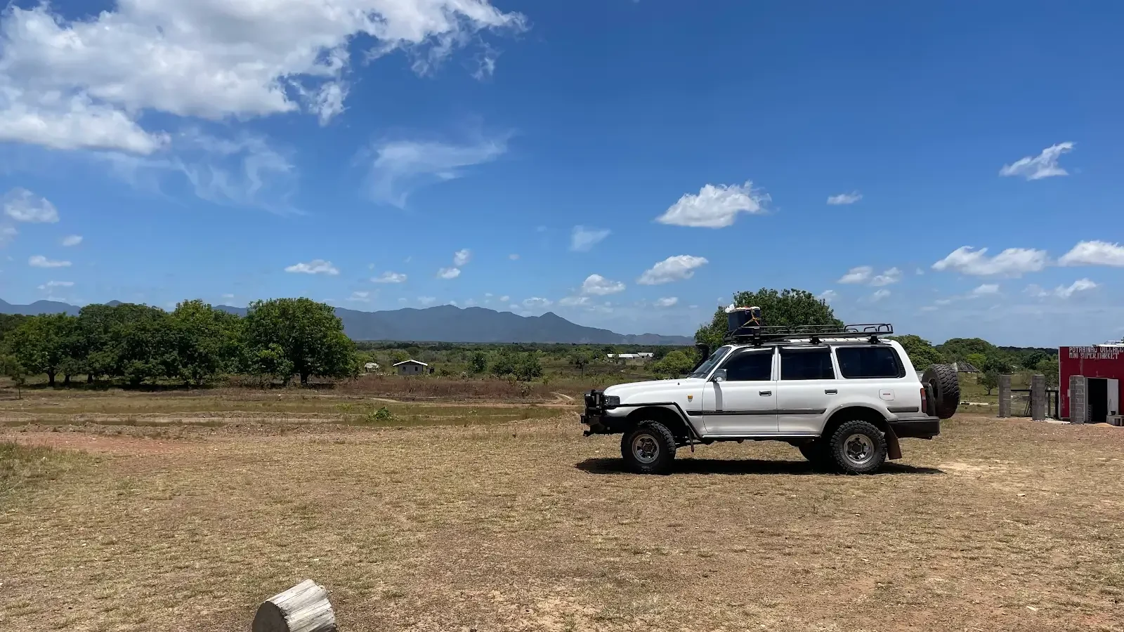 A silver four-wheel-drive vehicle stands in open savanna beneath a wide blue sky.