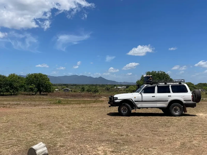 A silver four-wheel-drive vehicle stands in open savanna beneath a wide blue sky.